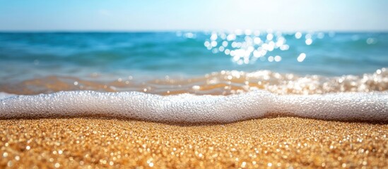 Fototapeta premium Close up of white foamy wave lapping on sandy beach, blue water, bright sunlight.