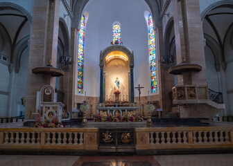 The interior of a church showcases stained glass windows casting colorful light on the altar....