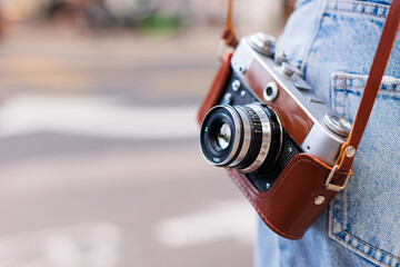 young girl in stylish clothes walks around the city and takes photographs with a film camera.