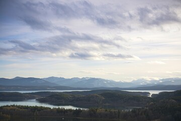 Fototapeta premium A scenic landscape view of a lake surrounded by mountains and forests under a cloudy sky
