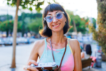 young girl in stylish clothes walks around the city and takes photographs with a film camera.