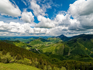 View of the Rozsutec mountain in the Mala Fatra mountains in Slovakia. The vast landscape features rolling green hills, dense forests, and a dramatic sky filled with large, bright clouds on a clear da