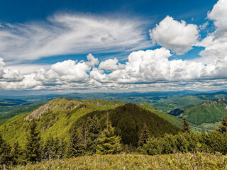 View of the Rozsutec mountain in the Mala Fatra mountains in Slovakia. The vast landscape features rolling green hills, dense forests, and a dramatic sky filled with large, bright clouds on a clear da