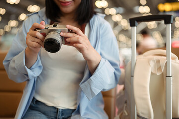 Smiling female traveler with her camera and suitcase sitting at the airport