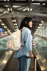Happy young woman traveler standing on the escalator with suitcase at airport terminal