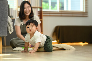 Fototapeta premium Adorable little baby boy learning to crawl with supportive mother closely watching. Child development concept