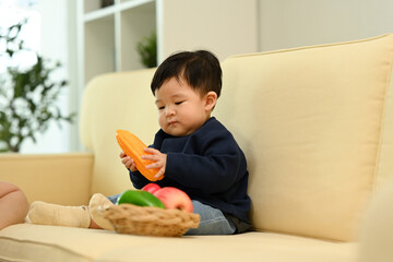 Little baby playing with vegetable toys on sofa at home. Child care concept