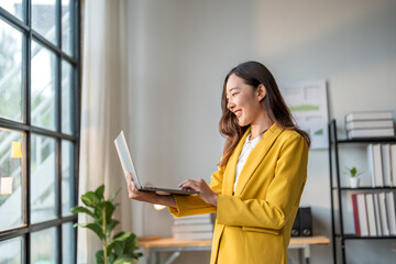 Young asian businesswoman smiling and typing on laptop in modern office