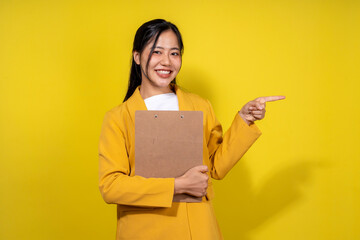 A woman in a yellow jacket holding a clipboard and pointing to the right