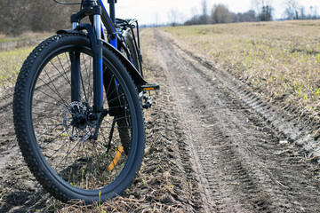 Fototapeta premium front wheel of a mountain bike. Mountain bike. stands on a field road. concept of cycling, repair or breakage, sports, outdoor activities. bike on trail, front wheel in focus. space for text