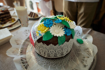 Two people are cutting a cake with knives, which is beautifully decorated with cookies, candies and fruits.