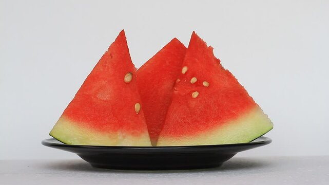 Some slices of watermelon (Citrullus lanatus) on black plate. Someone's hand takes a slice of watermelon, eat some of it, and put it back to the plate.