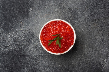 Red salmon caviar in a plate on a dark concrete background. Copy space. Snack delicacy.