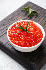 Red salmon caviar in a plate on a wooden cutting Board. Gray concrete background. Snack delicacy. Close up.