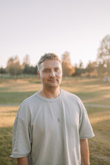 Portrait of happy Caucasian blonde man looking at camera outdoor, walking rest relax in spring green city park go down alley sunshine lawn outdoors on nature. Urban lifestyle leisure concept. High