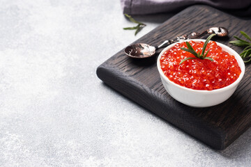 Red salmon caviar in a plate on a wooden cutting Board. Gray concrete background with Copy space. Snack delicacy.