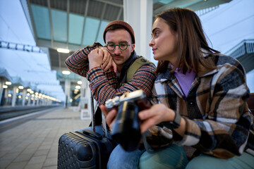 A young couple immersed in conversation while reviewing photos on a camera, enjoying a relaxed moment during their travels.