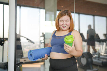 Fototapeta premium Obese asian woman in sportswear drinking protein shake from bottle After Overweight female exercising for weight loss Energy Vitality sportswoman wellness health