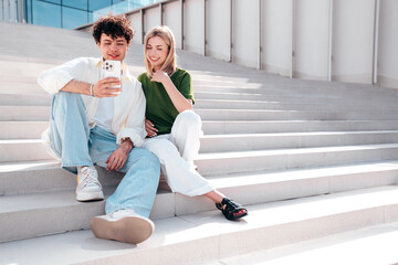 Smiling beautiful woman and her handsome boyfriend. Couple in casual summer clothes. Happy cheerful family. Female and man having fun. They posing in the street. Hold phone, use mobile apps, outdoor