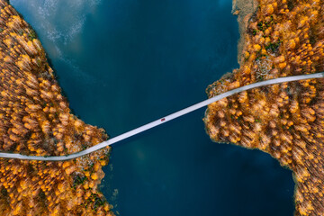 Aerial view of bridge road with red car over blue water lake or sea with island and autumn color woods in Finland.