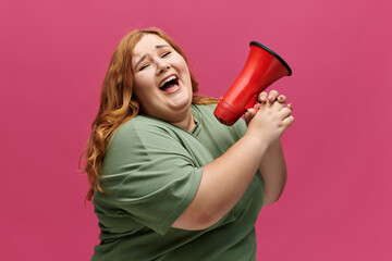 A plus-size woman in a green shirt holds a red megaphone, laughing while looking towards the camera.