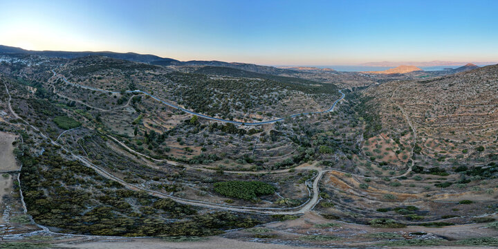 Aerial view of the historic Byzantine Road in Paros, Greece, winding through rugged hills, olive groves, and terraced fields, showcasing the island&rsquo;s ancient rural landscape at sunset.