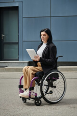 A woman sits in a wheelchair, focused on a tablet, in front of a sleek, modern building.