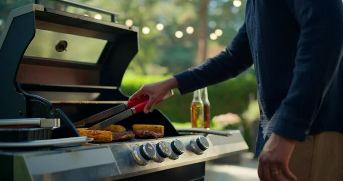 Black Man Standing Alone by the Barbecue Grill, Turning Food as It Cooks on Flame Griller. Close Up Portrait of a Young Male Enjoying a Quiet Moment, Focused on Preparing the Meal for a Garden Party