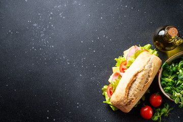 Sandwich with lettuce, cheese, tomatoes and ham on black kitchen table with ingredients for...