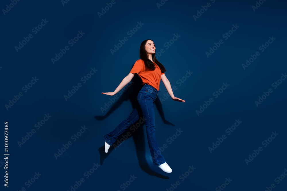 Wall mural Photo of gorgeous cheerful woman wear orange stylish clothes walk empty space isolated on dark blue color background