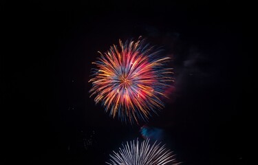 Obraz premium A colorful firework display bursts across the night sky, a mix of red, blue, and yellow sparks reaching out in vibrant tendrils.