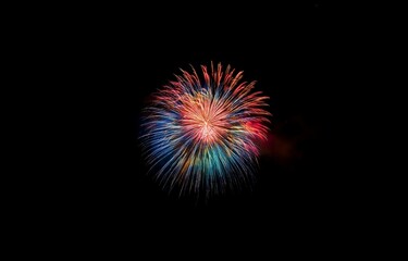 Fototapeta premium A single firework explodes in the night sky, radiating colorful sparks.