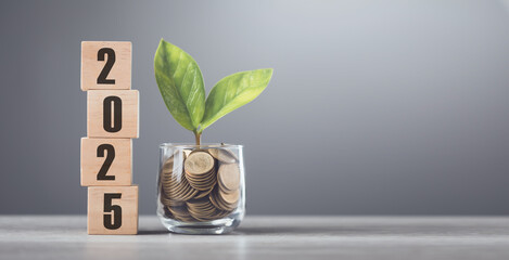 2025 is written on a wooden block next to a glass jar filled with coins, placed on a wooden table...