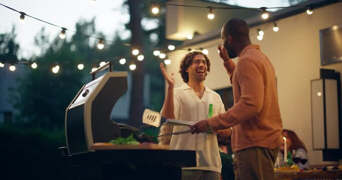 Diverse Young Adult Men Spending Time Together at an Outdoors Garden Barbecue Party. Multiethnic Friends Grilling BBQ Meat, Drinking Beer and Casually Chatting on a Warm Evening