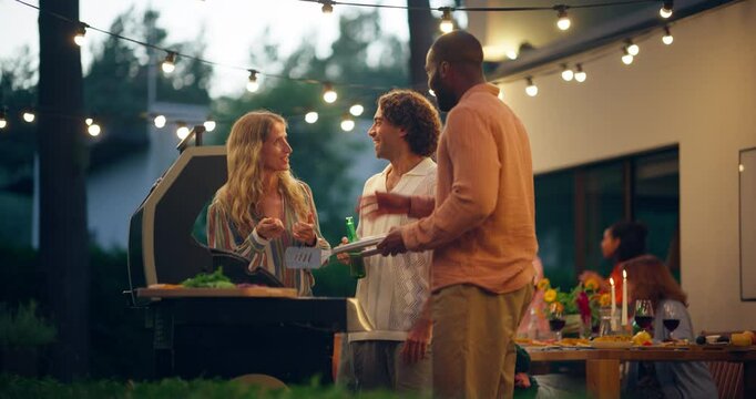 Three Happy Adult Friends Gathered Around a Fire Grill, Chatting and Telling Funny Stories while Preparing Barbecue Beef Steak. Friends Spending Time Outdoors, Talking, Relaxing, Drinking Beers