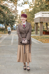 A brunette in vintage clothes and a hat stands on a path in an autumn park. Retro style
