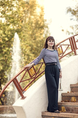 A young woman fashionably dressed in a vintage straw hat walks in an autumn park.