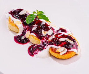 Delicious cottage cheese pancakes lying on white plate with berry sauce and mint
