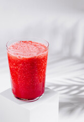Red smoothie in a glass is standing on white cube on white background