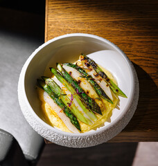 Grilled asparagus lying on creamy polenta in white bowl on wooden table