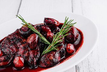 Delicious duck breast covered in cherry sauce with rosemary sprig on white plate