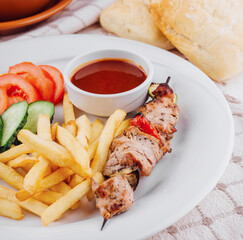 Grilled pork skewer with french fries and tomato sauce served on a plate