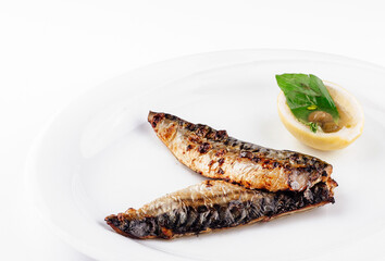 Grilled mackerel fillets served on white plate with lemon and basil garnish