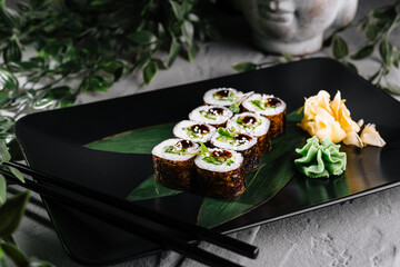 Delicious sushi rolls served on black plate with wasabi and ginger