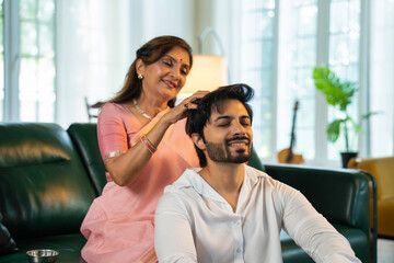 Elderly Indian woman giving her young son a head massage with oil in a cozy, modern home