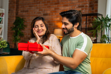 Elderly Indian mother and her son share laughter and gifts with a beautiful rose bouquet