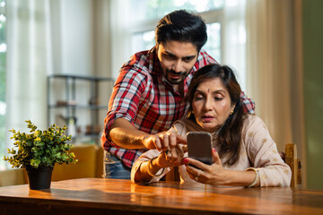 Elderly Indian mother and son viewing photos or video calling on a smartphone in cozy lighting