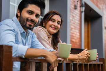 Elderly Indian mother and her son savoring coffee while enjoying views from the gallery railing