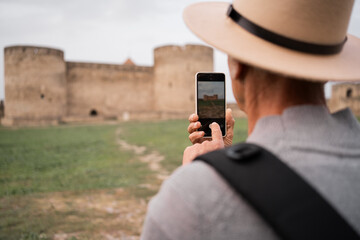 Tourist photographing ancient fortress takes close-up shot of castle using smartphone, capturing architectural details and historical atmosphere during travel exploration of historic site.