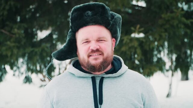 Portrait of a man with a beard, wearing a winter hat with earflaps. A close-up of a man looking at the camera with a smile.